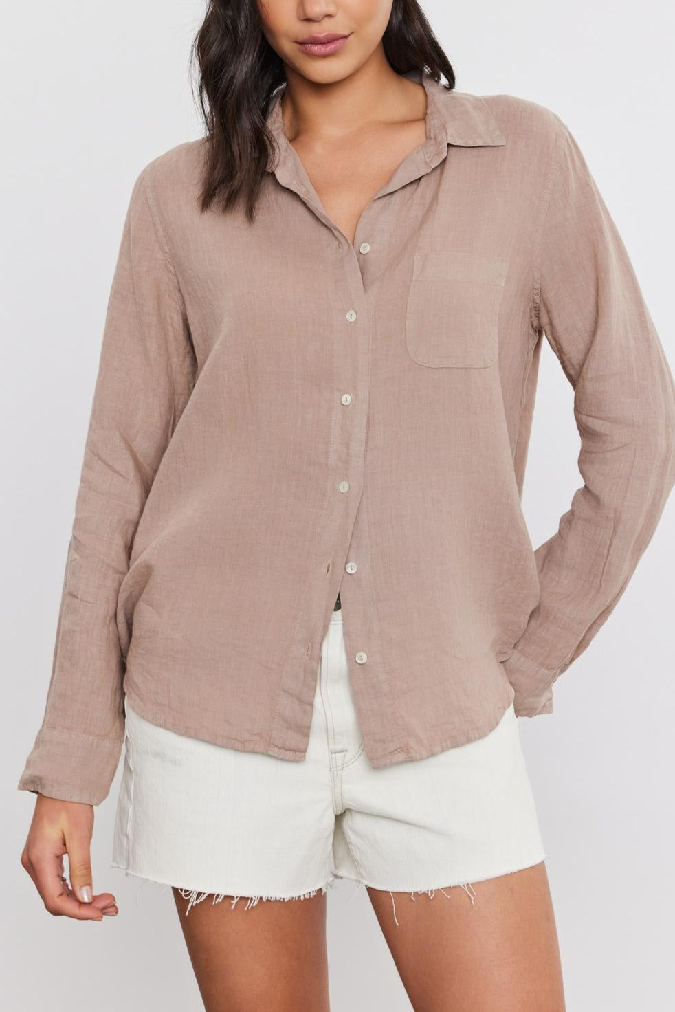 A woman with shoulder-length dark hair wearing a casual beige Velvet by Graham & Spencer Natalia Linen Button-Up Shirt and white frayed shorts, both in a relaxed silhouette.-36752935813313