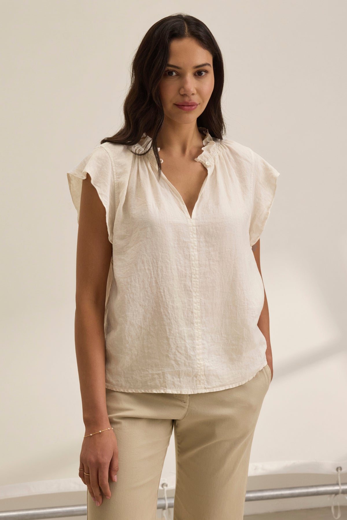 Against a plain backdrop, a person wears beige pants paired with the SEMIRA LINEN TOP, featuring light, short sleeves and flutter detailing. The top is from Velvet by Graham & Spencer.