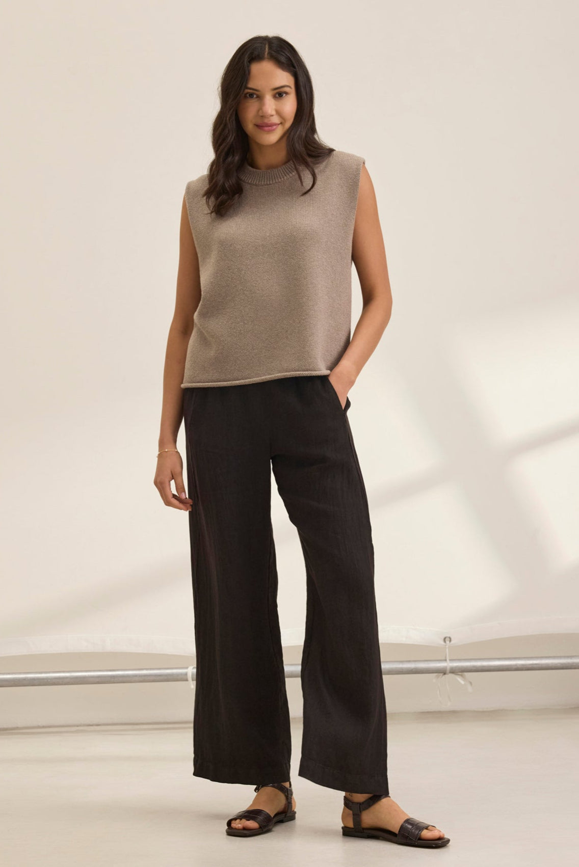 A woman smiles in a beige sleeveless top and the STEPHANIE LINEN PANT by Velvet by Graham & Spencer, featuring an elastic waist design, with sandals, posing against a plain white background.-38819778461889