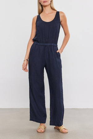 A woman in a dark blue Velvet by Graham & Spencer Winnie Linen Jumpsuit stands against a plain background, looking directly at the camera with her hands at her sides.