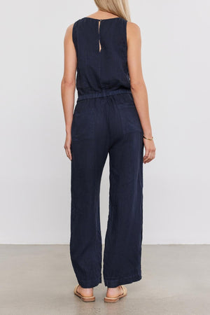 A woman seen from behind, wearing a Velvet by Graham & Spencer WINNIE LINEN JUMPSUIT and tan shoes, standing in front of a plain background.