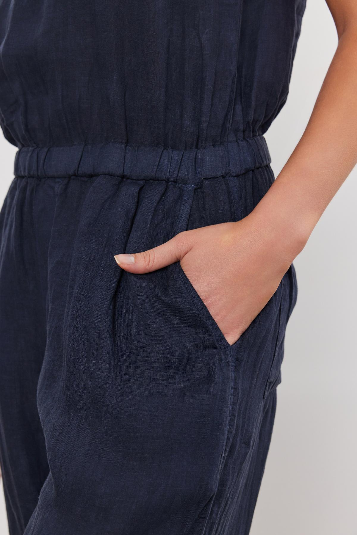 A close-up of a person's hand resting in the pocket of a WINNIE LINEN JUMPSUIT by Velvet by Graham & Spencer, highlighting the garment's texture and elastic waist detail.