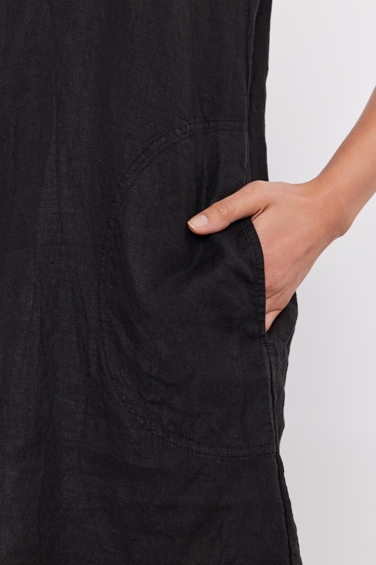 Close-up of a hand inserted into the pocket of a black YESSIE LINEN DRESS by Velvet by Graham & Spencer, focusing on the texture and stitching details.-36910019150017