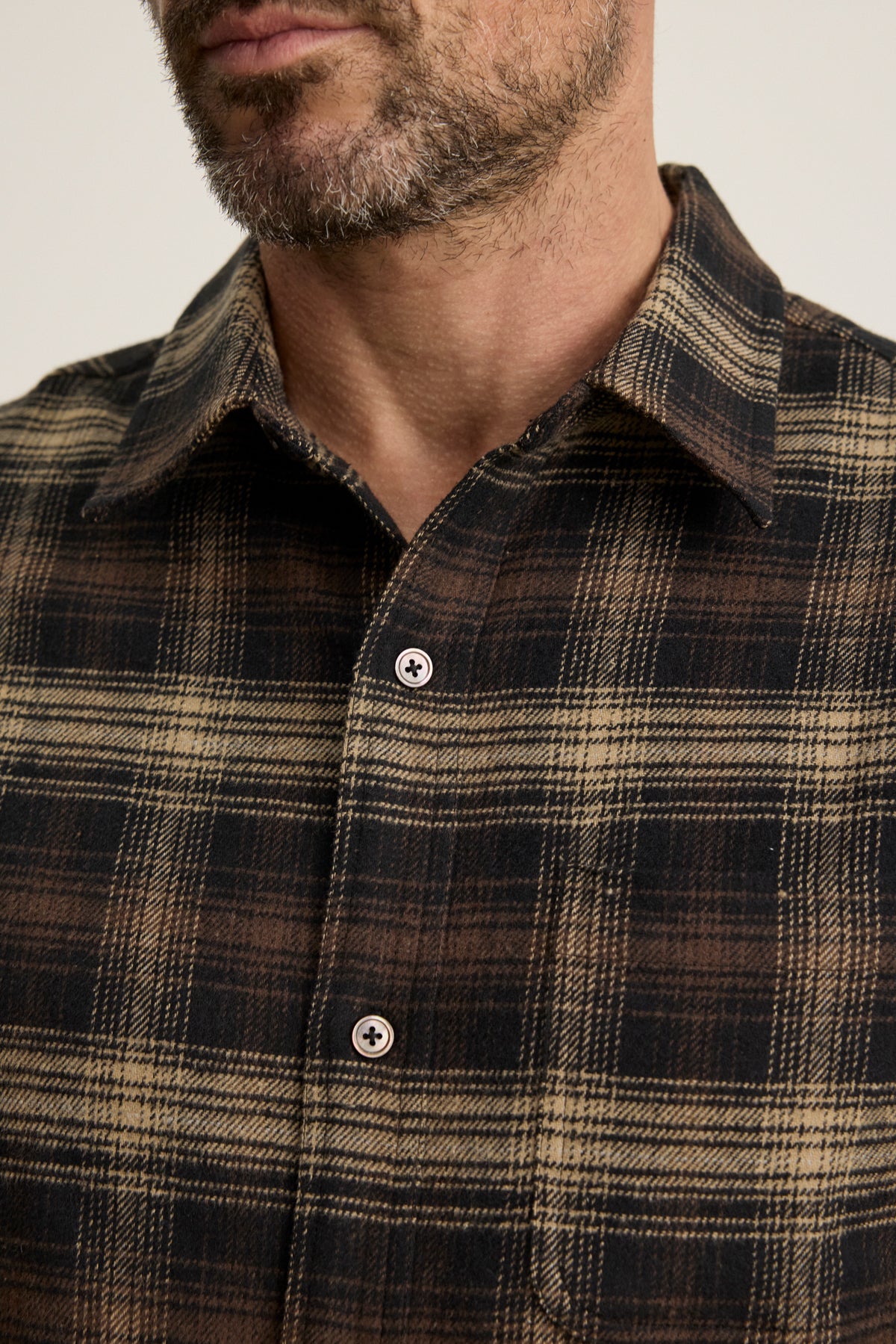 Close-up of a man in the BRYANT BUTTON-UP SHIRT by Velvet by Graham & Spencer, a brown and black plaid cotton flannel with a classic collar, showing his chest and part of his bearded face.