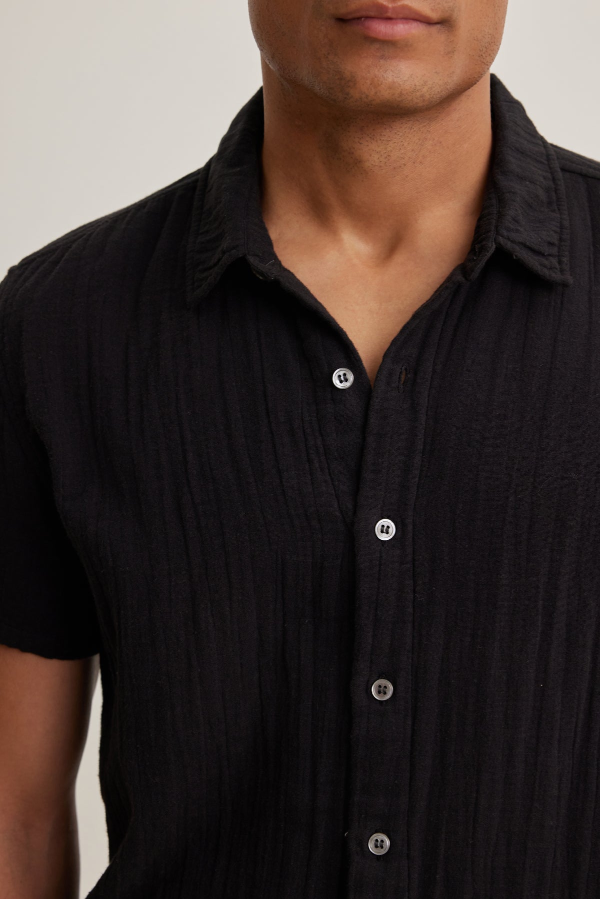 A person wears the Velvet by Graham & Spencer CHRISTIAN Cotton Gauze Button-Up Shirt, a short-sleeved textured black top, shown from shoulders to mid-torso against a plain background.