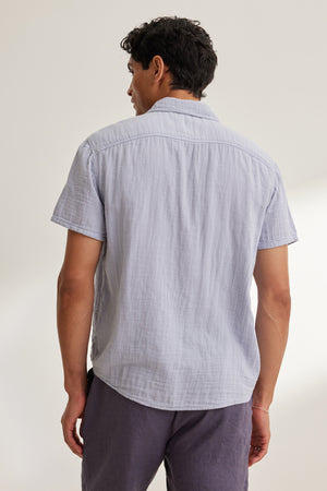A man faces away from the camera wearing the CHRISTIAN COTTON GAUZE BUTTON-UP SHIRT by Velvet by Graham & Spencer, paired with dark shorts against a plain background.