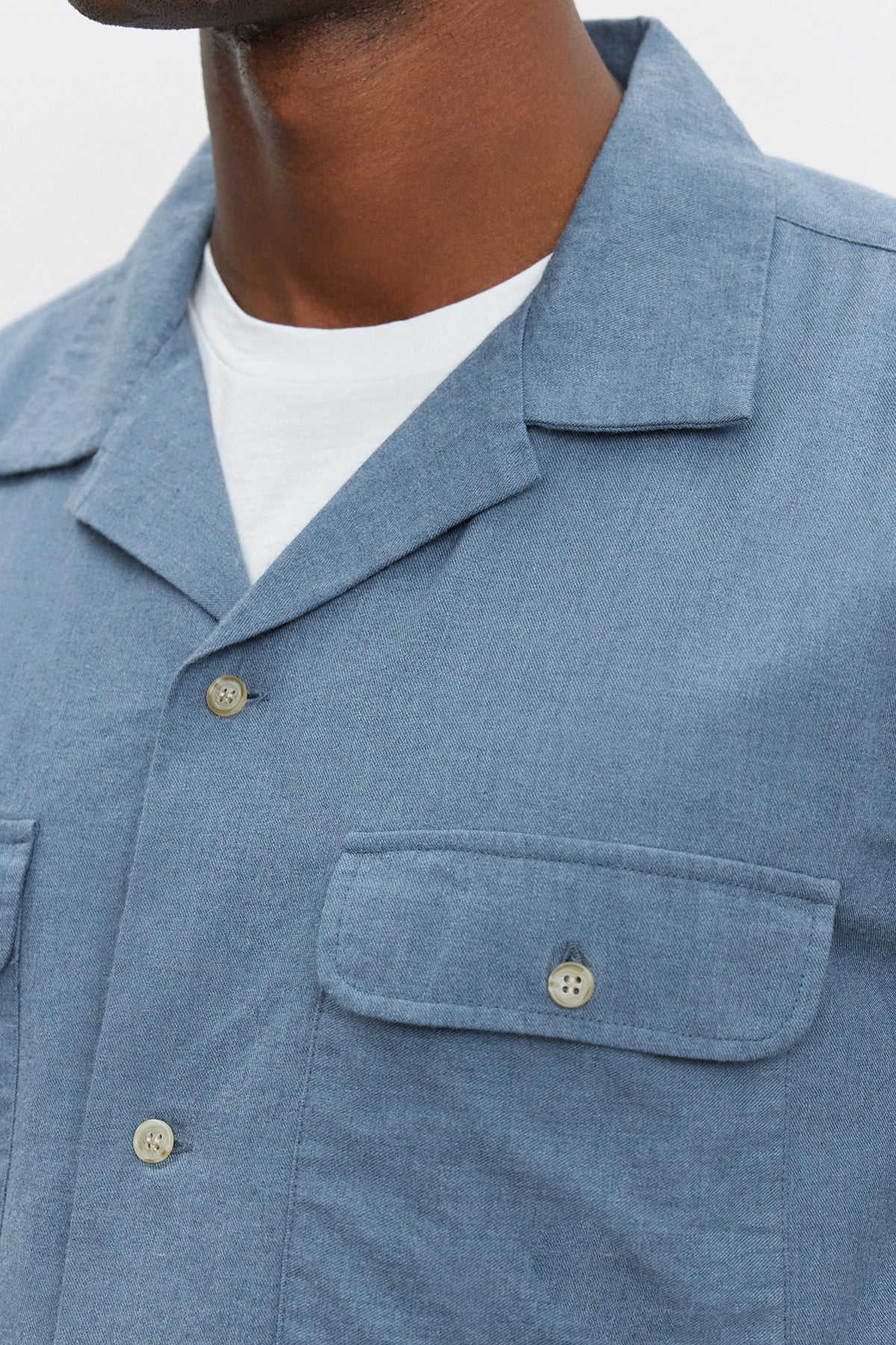 Close-up of a person wearing the DONOVAN BUTTON-UP SHIRT by Velvet by Graham & Spencer in light blue with a white undershirt. This cotton blend twill shirt features two pockets with buttoned flaps on the chest.