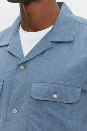 Close-up of a person wearing the DONOVAN BUTTON-UP SHIRT by Velvet by Graham & Spencer in light blue with a white undershirt. This cotton blend twill shirt features two pockets with buttoned flaps on the chest.