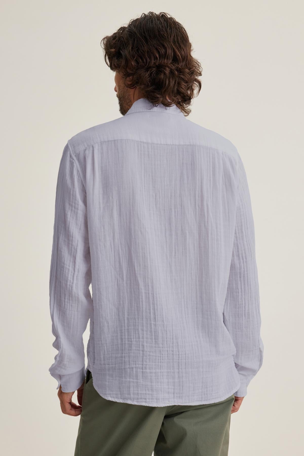 With curly hair, a person faces away from the camera, wearing green pants and the versatile ELTON COTTON GAUZE BUTTON-UP SHIRT by Velvet by Graham & Spencer.-38658658566337