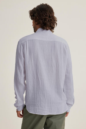 With curly hair, a person faces away from the camera, wearing green pants and the versatile ELTON COTTON GAUZE BUTTON-UP SHIRT by Velvet by Graham & Spencer.