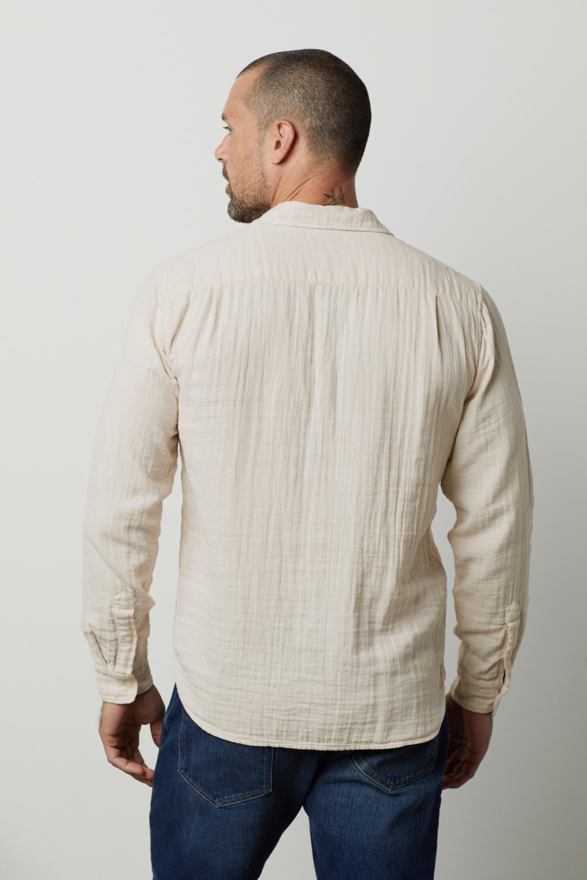   A man viewed from behind, wearing a Velvet by Graham & Spencer Elton Cotton Gauze Button-Up Shirt and blue jeans, standing against a white background. 