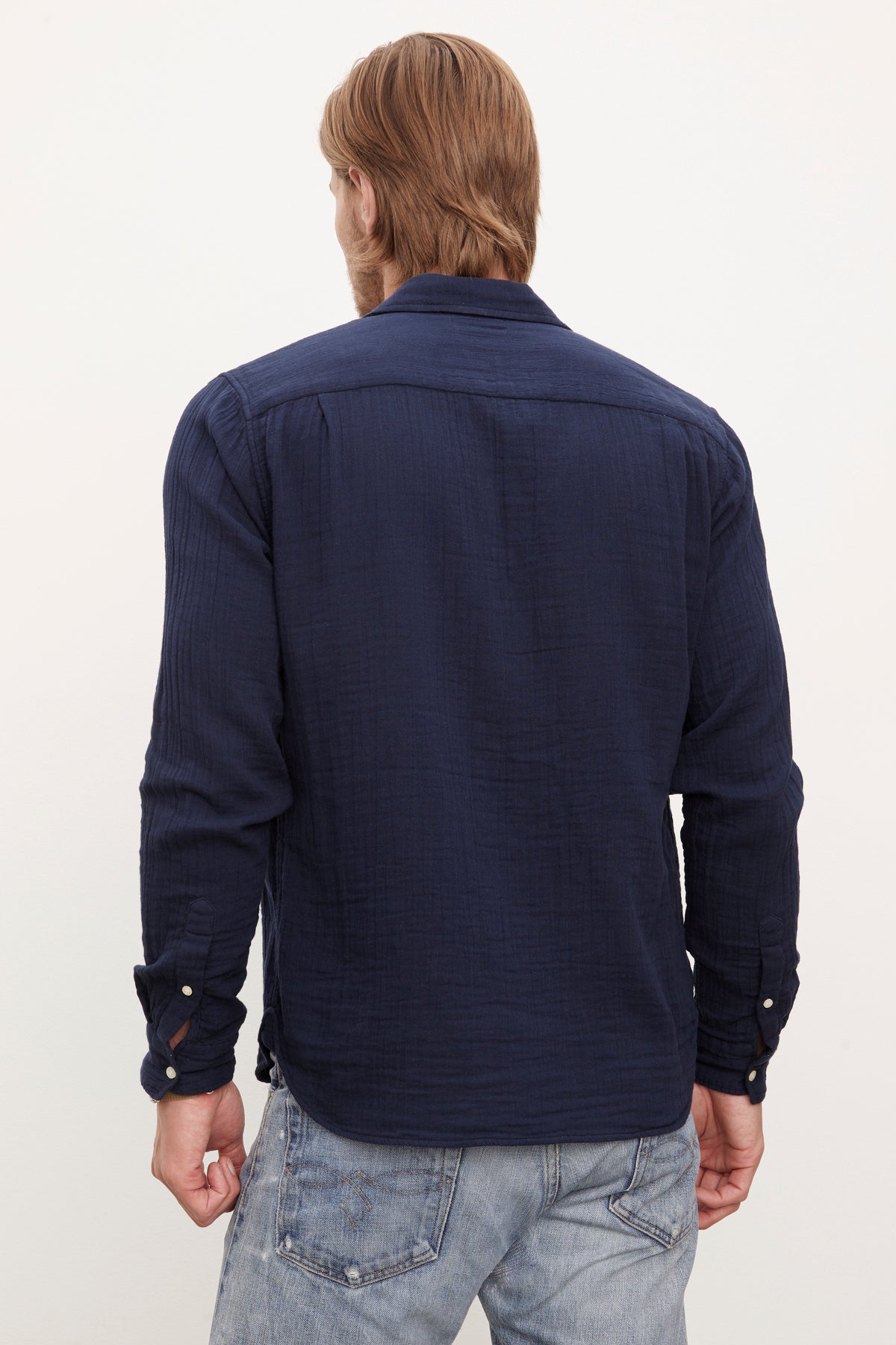 A man viewed from the back wearing a Velvet by Graham & Spencer ELTON COTTON GAUZE BUTTON-UP SHIRT with double button cuffs and faded blue jeans.-36009394995393