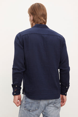 A man viewed from the back wearing a Velvet by Graham & Spencer ELTON COTTON GAUZE BUTTON-UP SHIRT with double button cuffs and faded blue jeans.