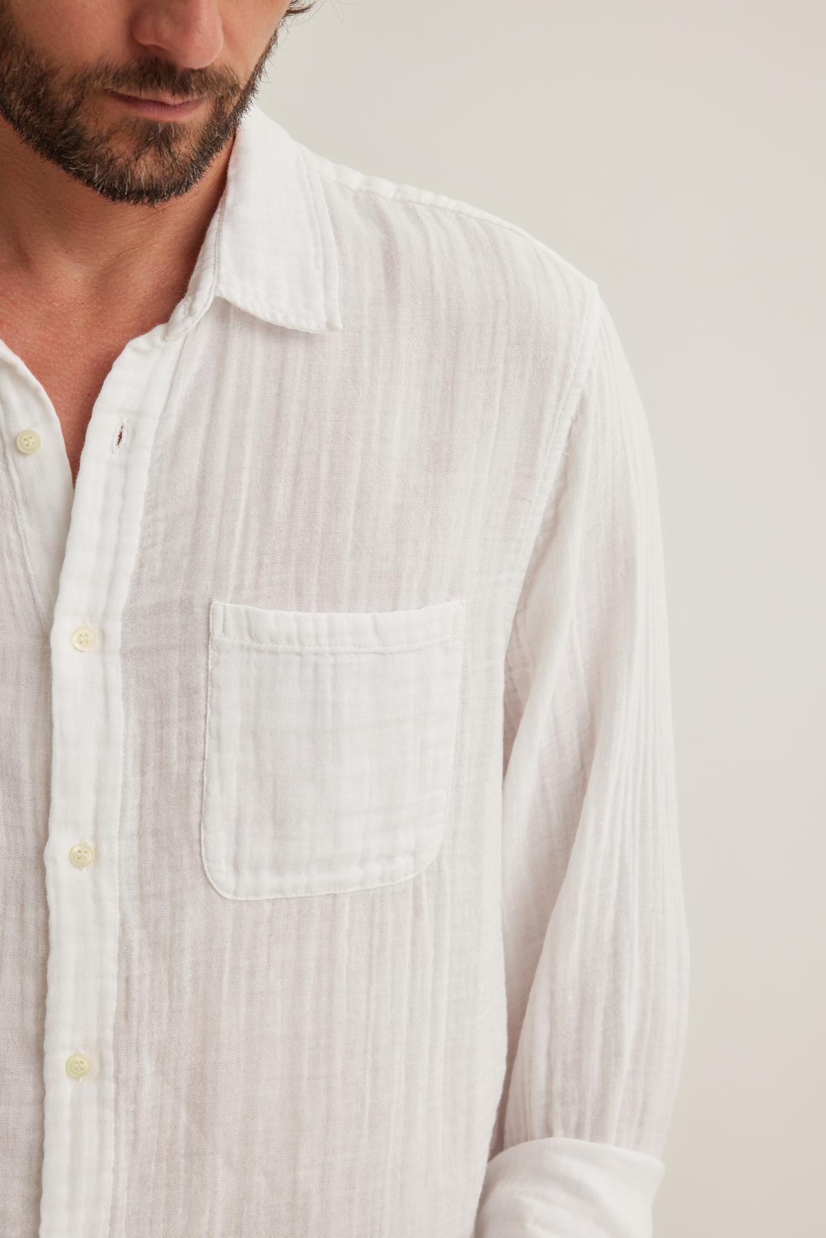 A person wearing the ELTON COTTON GAUZE BUTTON-UP SHIRT by Velvet by Graham & Spencer, featuring a white textured cotton gauze fabric, chest pocket, and cropped shoulders and neck, stands against a plain background.-38643274121409