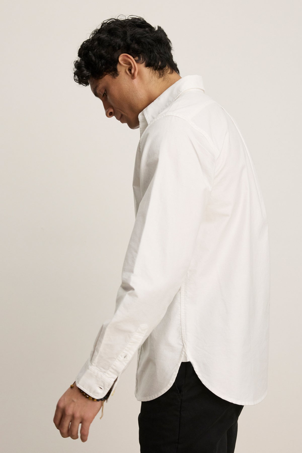 A person with short dark hair, dressed in the EMMETT BUTTON-DOWN SHIRT by Velvet by Graham & Spencer and black pants, stands sideways against a plain light background.