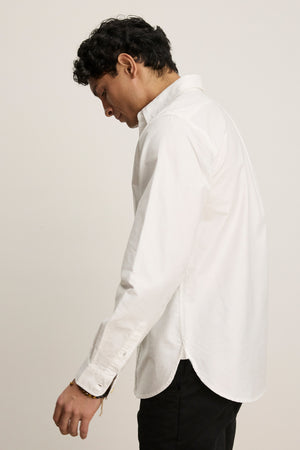 A person with short dark hair, dressed in the EMMETT BUTTON-DOWN SHIRT by Velvet by Graham & Spencer and black pants, stands sideways against a plain light background.