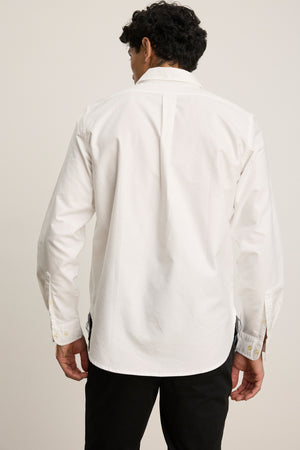A man is seen from behind against a plain background, wearing the EMMETT BUTTON-DOWN SHIRT by Velvet by Graham & Spencer—a classic long-sleeve white cotton oxford paired with black pants for timeless style.