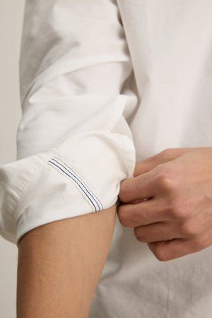 Rolling up the sleeve of the EMMETT BUTTON-DOWN SHIRT by Velvet by Graham & Spencer, a person reveals part of their forearm and hand.