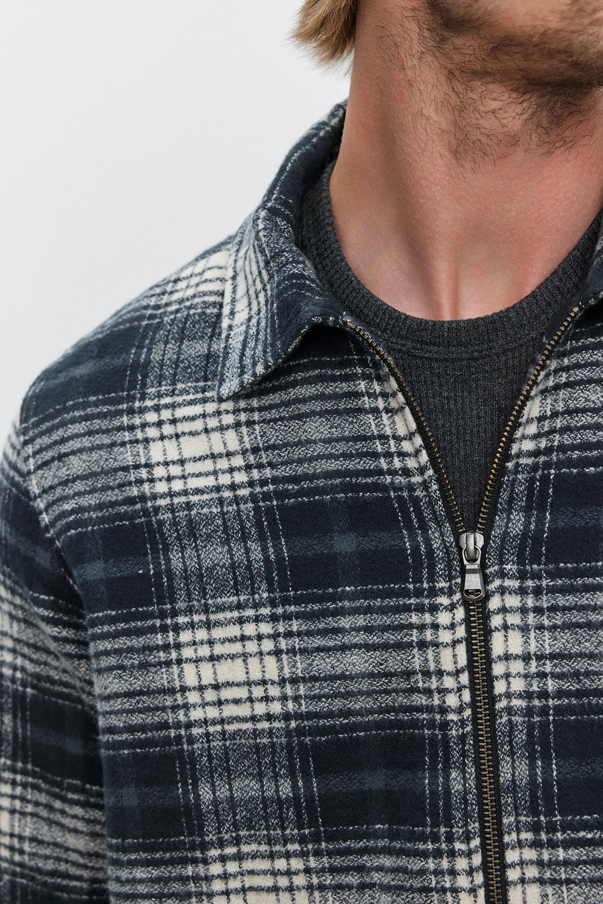 Close-up of a person wearing the KEITH SHIRT, a plaid cotton blend flannel jacket with a classic collar and zipper front from Velvet by Graham & Spencer, over a dark shirt. The person’s face is partially out of the frame.-37893904892097