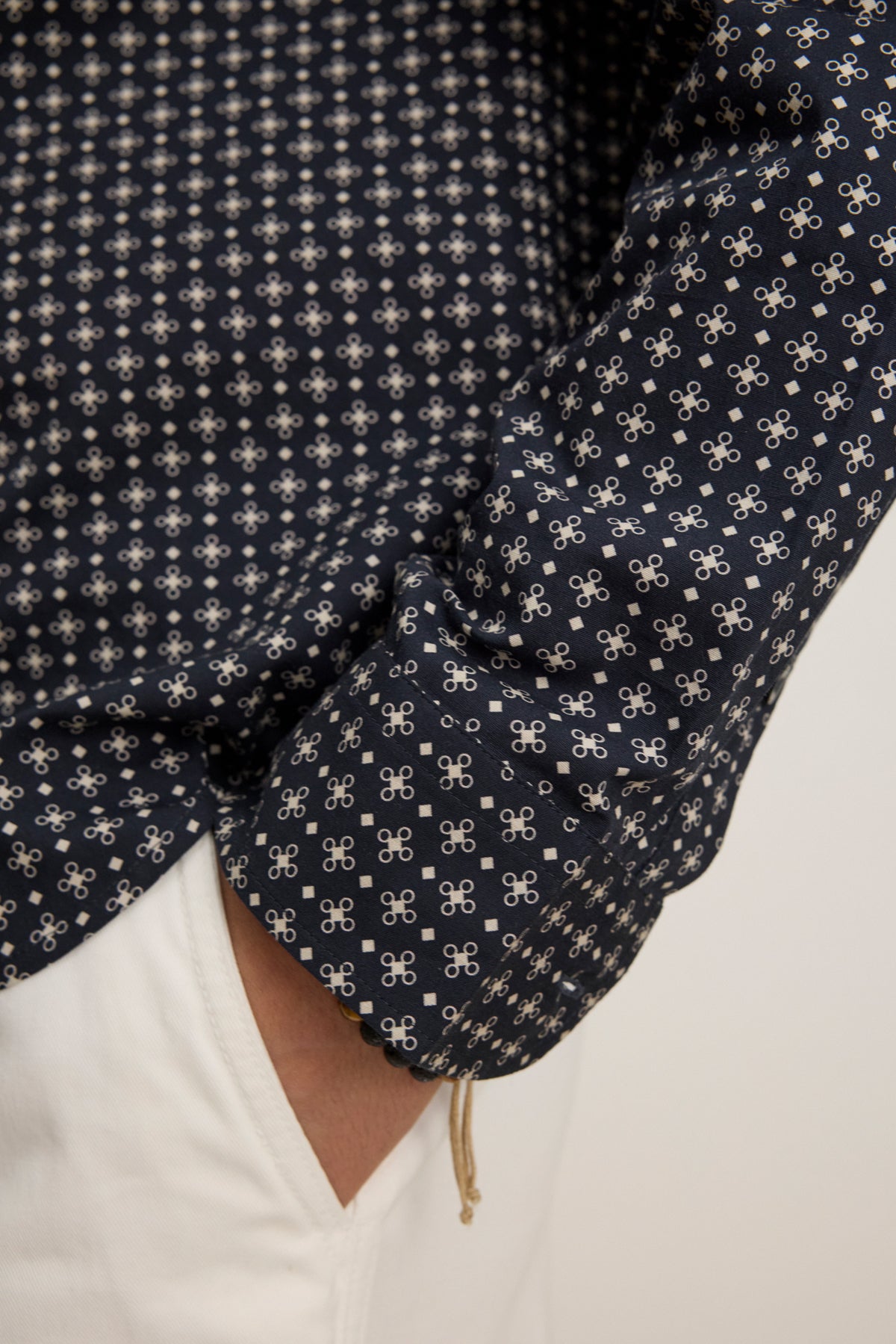 Close-up of a person wearing the LAWRENCE BUTTON-UP SHIRT by Velvet by Graham & Spencer, featuring a classic fit and navy blue pattern with white designs, paired with white pants and their hand in their pocket.