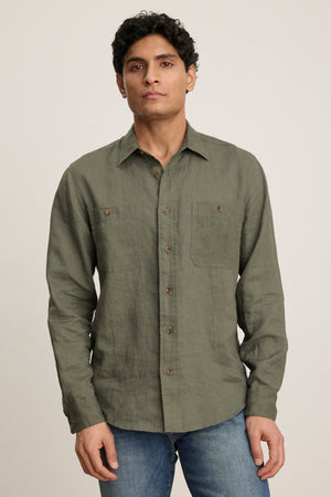A person faces forward in a Velvet by Graham & Spencer LINDEN LINEN BUTTON-UP SHIRT in olive green, paired with blue jeans, against a plain light background.