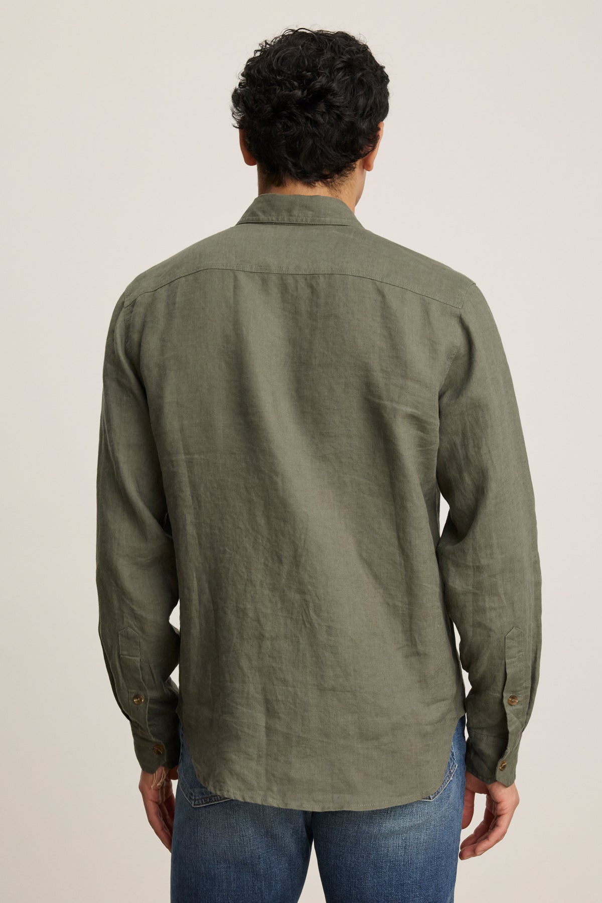 A person is seen from the back wearing the Velvet by Graham & Spencer LINDEN LINEN BUTTON-UP SHIRT in olive green with long sleeves and a button front, paired with blue jeans, against a plain background.