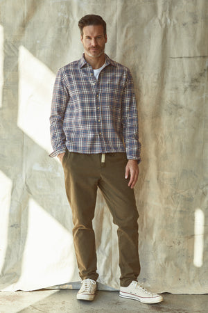 A man standing in front of a wall in a Velvet by Graham & Spencer STAN PLAID BUTTON-UP SHIRT.