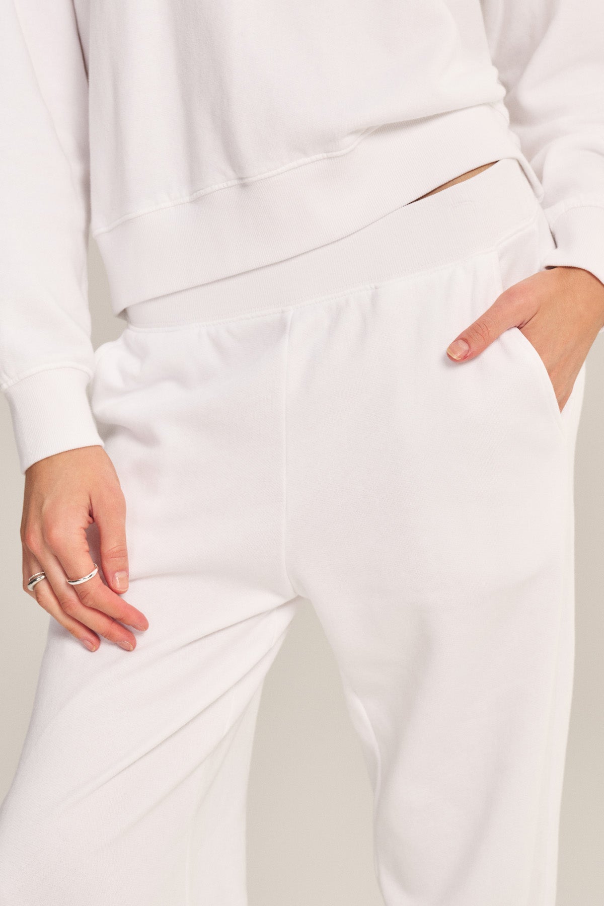 A person wearing the YOKO SWEATSHIRT by Velvet by Graham & Spencer, paired with white sweatpants and one hand in the pocket, photographed from mid-torso to thigh.-40293969297601
