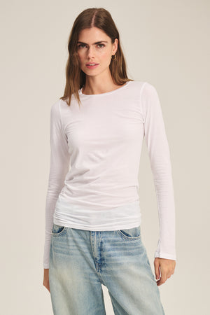 A person wears the ZOFINA TEE by Velvet by Graham & Spencer—a fitted long sleeve crewneck—paired with light blue jeans, facing the camera against a neutral background.