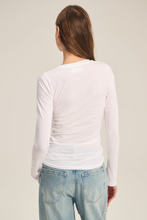 A person is shown from the back against a neutral background wearing the Velvet by Graham & Spencer ZOFINA TEE in white—an ultra-soft, long-sleeve crewneck top—paired with light blue jeans.