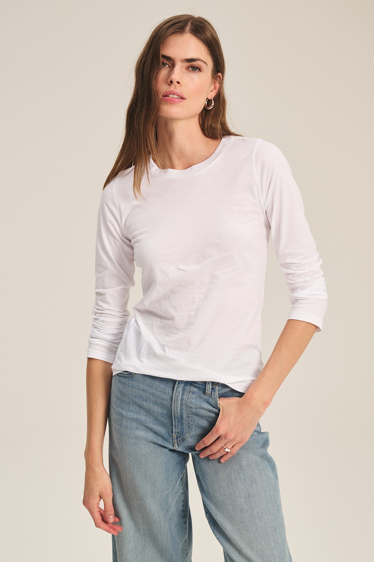 A woman stands against a plain, light background wearing the ZOFINA TEE by Velvet by Graham & Spencer—an ultra-soft, fitted long sleeve crewneck—paired with light blue jeans.-39601037082817