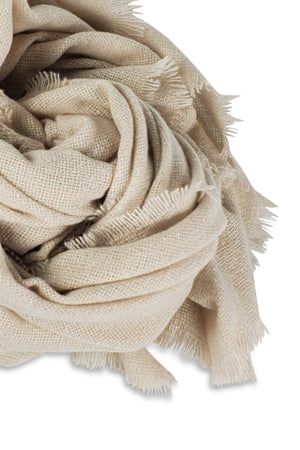 Close-up of the COZY SOLID SCARF by Velvet by Graham & Spencer, a loosely folded beige jumbo scarf with frayed edges, perfect for winter style, displayed on a white background.