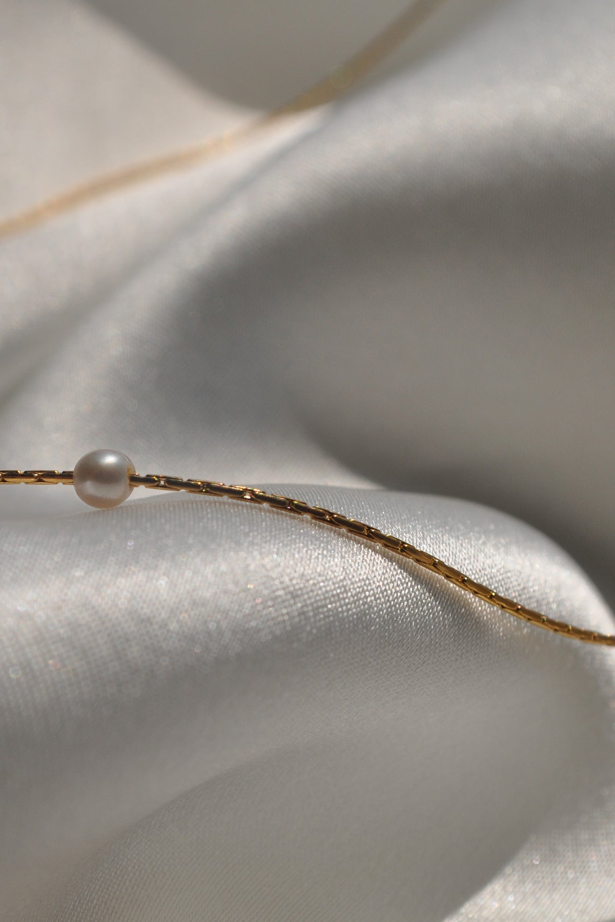 The MINA NECKLACE BY THATCH, featuring delicate freshwater pearls, rests on smooth, shimmering white fabric.