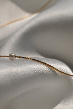 The MINA NECKLACE BY THATCH, featuring delicate freshwater pearls, rests on smooth, shimmering white fabric.