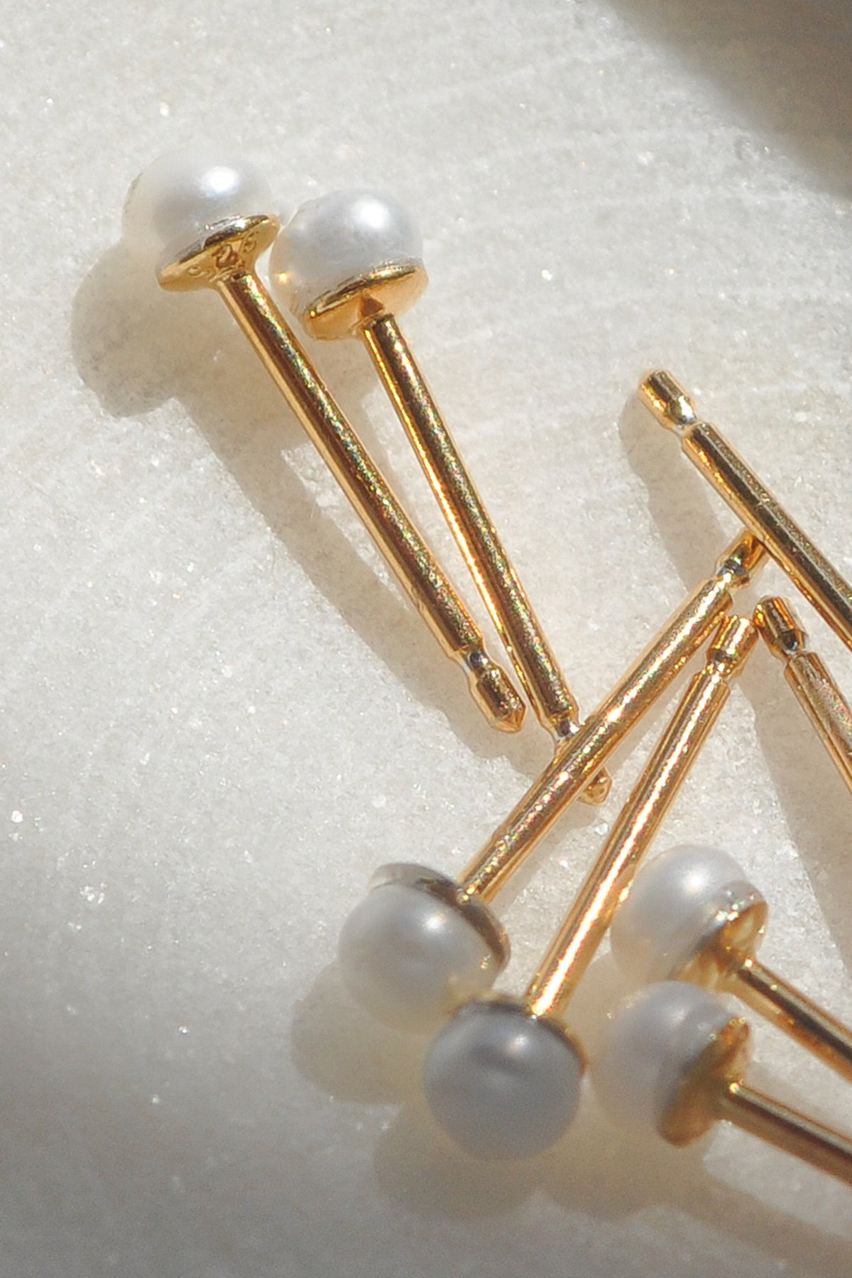 MINA STUD EARRINGS BY THATCH feature gold pins with white pearl-like heads on a light textured surface, reminiscent of Thatch jewelry collection pieces.-15203629039809