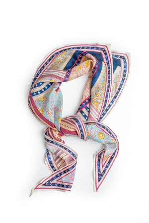The DIAMOND SHAPE SILK SCARF by Velvet by Graham & Spencer features a colorful, intricate pattern with shades of blue, pink, and white, arranged in a loose loop on a white background—perfect to style as a chic bandana.