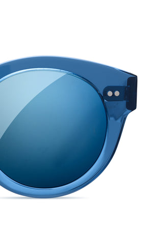 Close-up of the upper left portion of CHIMI EYEWEAR 003 by Chimi, featuring blue, round sunglasses with a transparent plastic frame and mirrored blue lens—premium European-made quality eyewear.