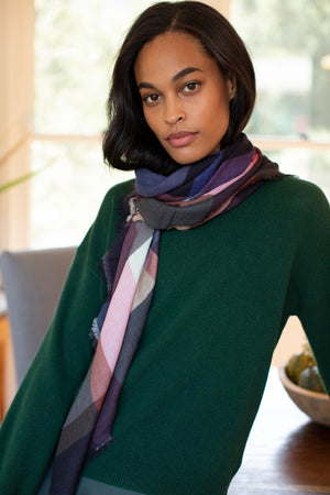 A woman with shoulder-length dark hair, wearing a green sweater and the PLAID WOOL BLEND SCARF BY EPICE from Epice, stands indoors facing the camera.