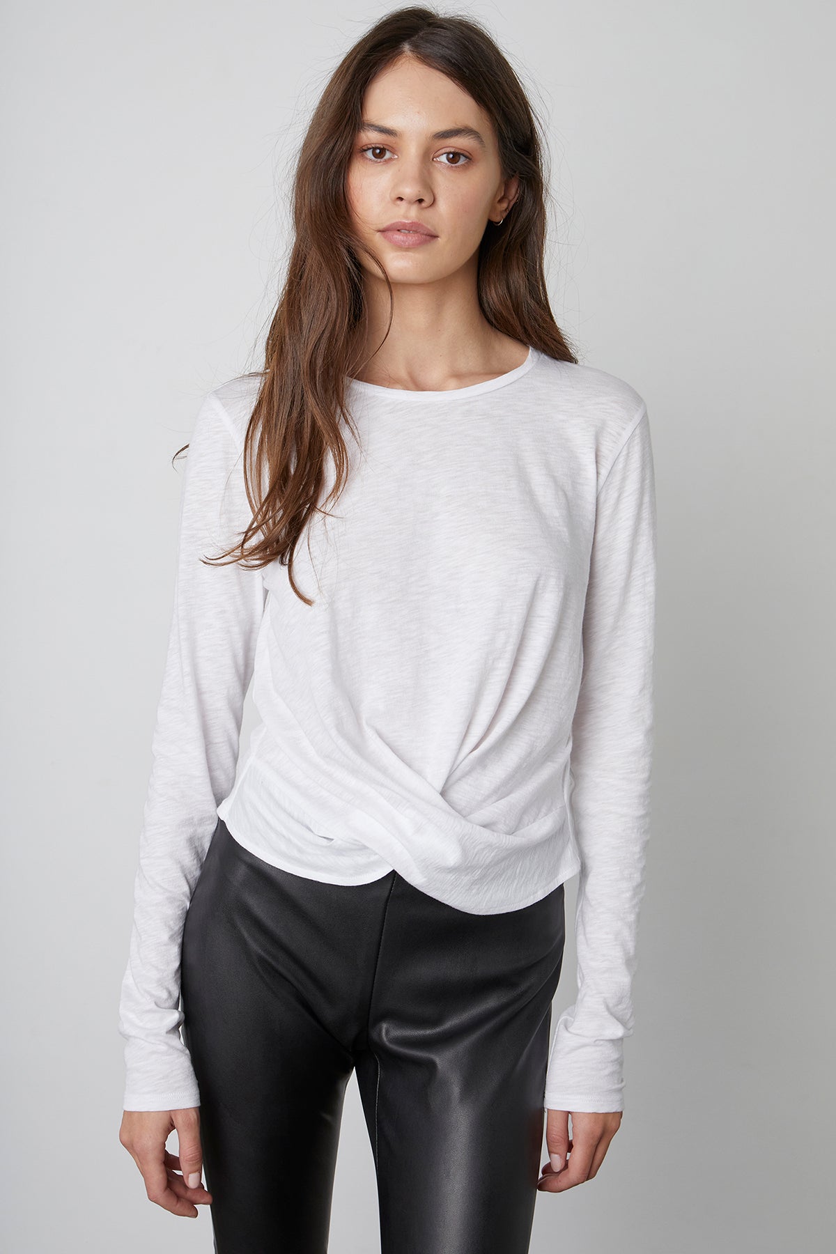 The model is wearing a Velvet by Graham & Spencer BEATRICE FRONT TWIST TEE and black leather pants, giving her outfit a relaxed yet feminine appeal.-23119086584001