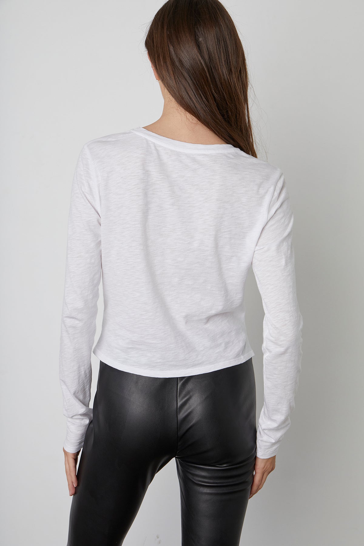 The back view of a feminine woman wearing leather leggings and a BEATRICE FRONT TWIST TEE by Velvet by Graham & Spencer that accentuates her waist.-23119086551233