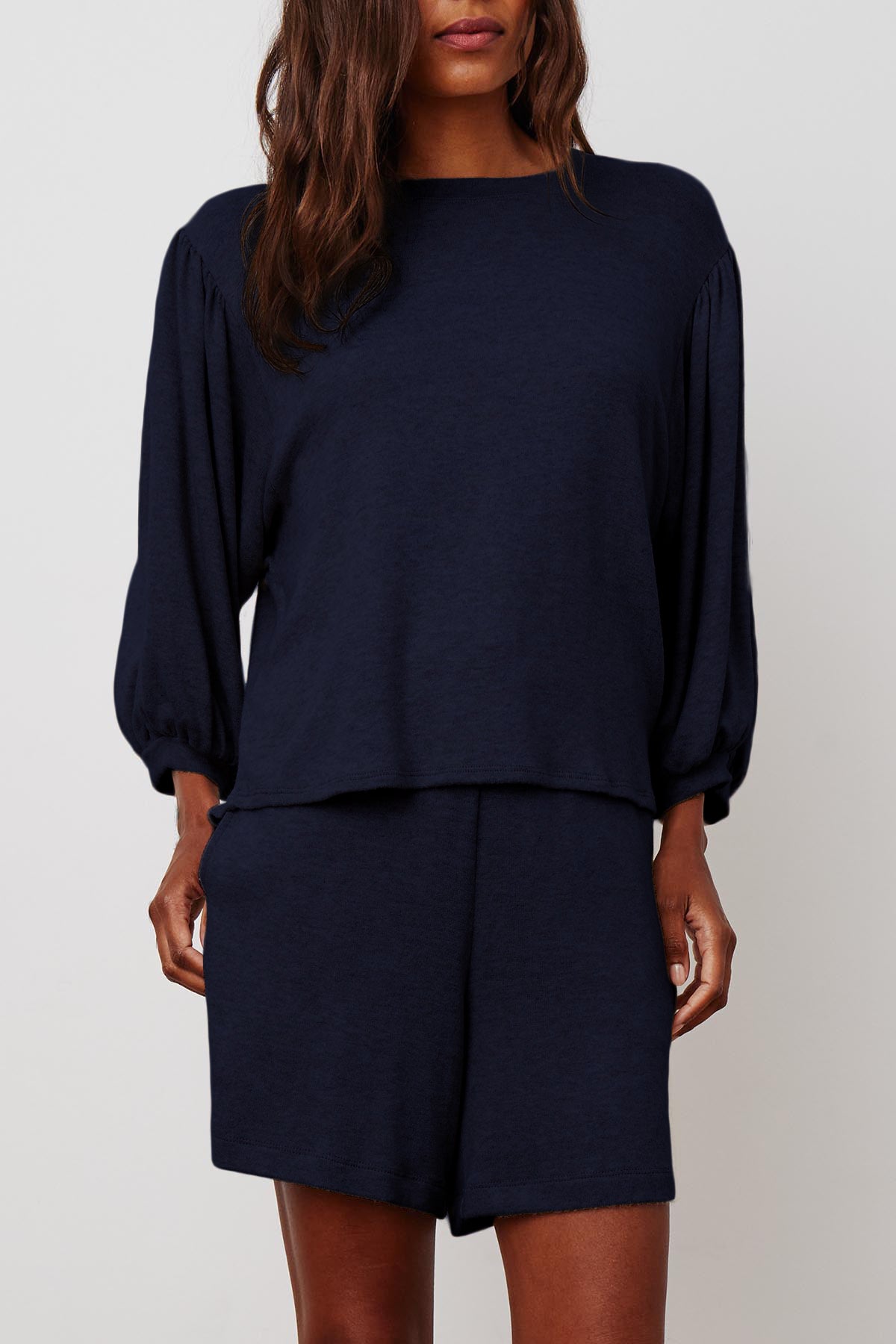 A person wearing a soft cotton knit, long-sleeve, loose-fitting navy top and matching navy JANEY DRAWSTRING SHORT by Velvet by Graham & Spencer with an elastic waist. Their hair is long and wavy.