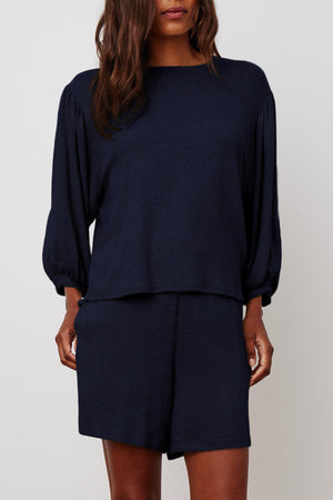 A person wearing a soft cotton knit, long-sleeve, loose-fitting navy top and matching navy JANEY DRAWSTRING SHORT by Velvet by Graham & Spencer with an elastic waist. Their hair is long and wavy.