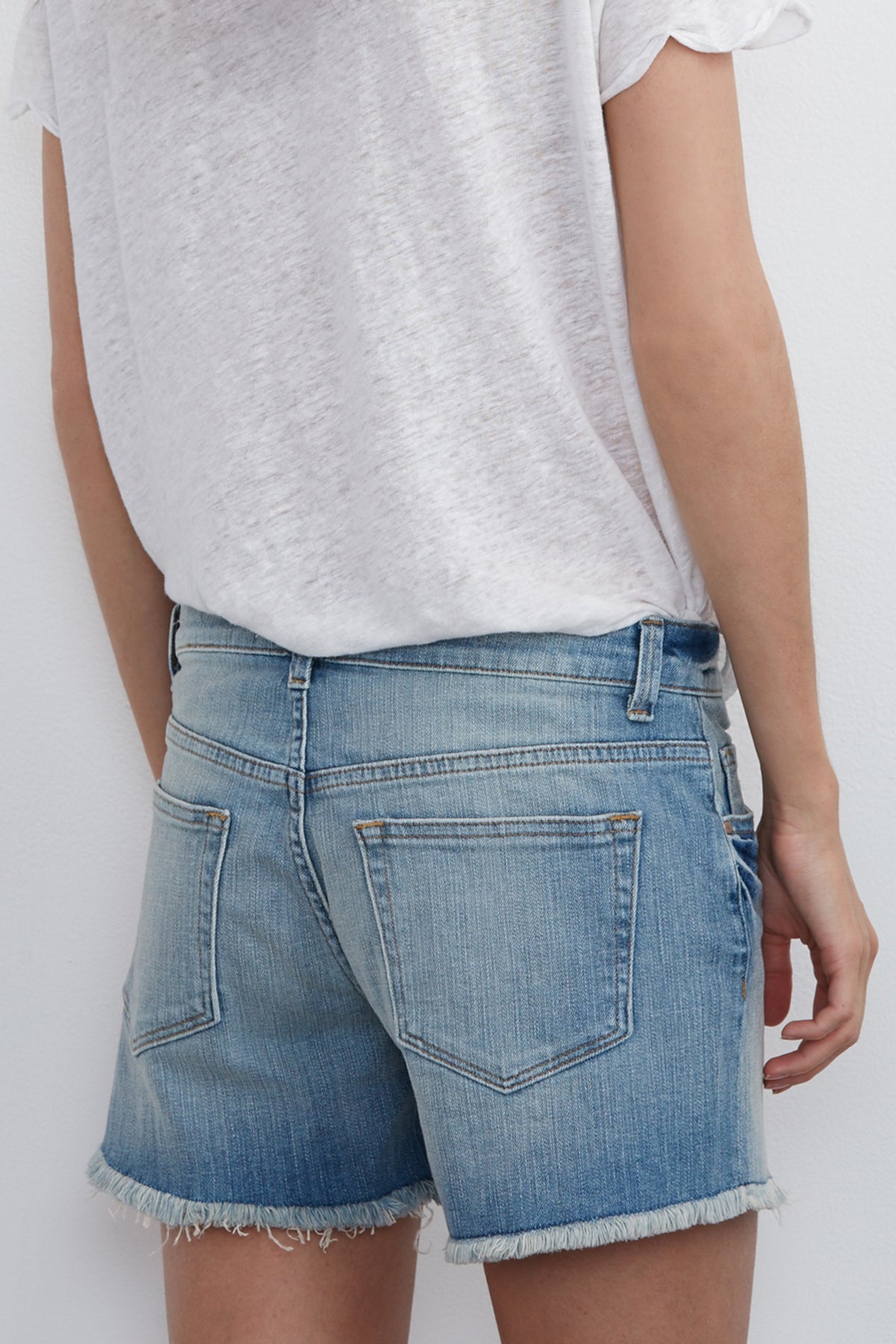 A person wearing a white t-shirt and Velvet by Graham & Spencer's Cindy Frayed Hem Boyfriend Shorts in blue, viewed from the back.