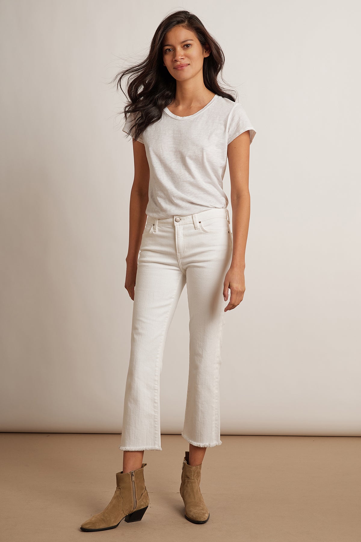 A person with long hair stands against a plain background, wearing a white T-shirt, TWIGGY HIGH RISE CROP JEAN by Velvet by Graham & Spencer, and tan boots.-1202293735505