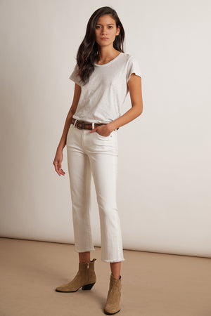 A person stands against a plain background wearing a white T-shirt, Velvet by Graham & Spencer TWIGGY HIGH RISE CROP JEANS with frayed hems, a brown belt, and tan ankle boots.