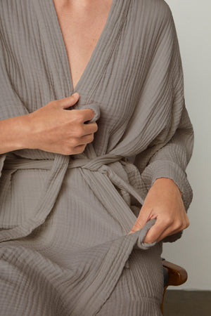 a woman wearing a Jenny Graham Home COTTON GAUZE ROBE sitting on a chair.