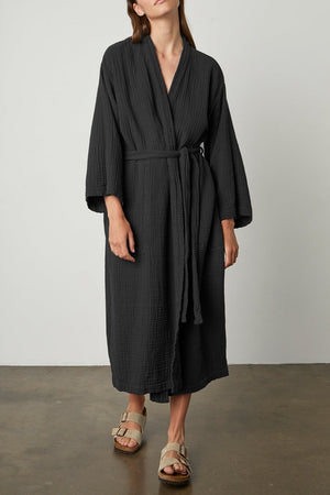 A woman wearing a black Cotton Gauze Robe by Jenny Graham Home and sandals.