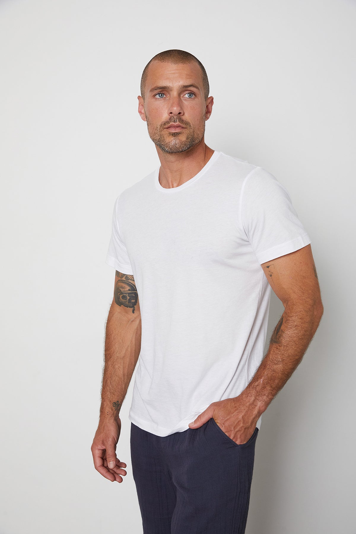 White Angelo crew neck graphic tee, model standing with hand in pocket of Ryan pant.