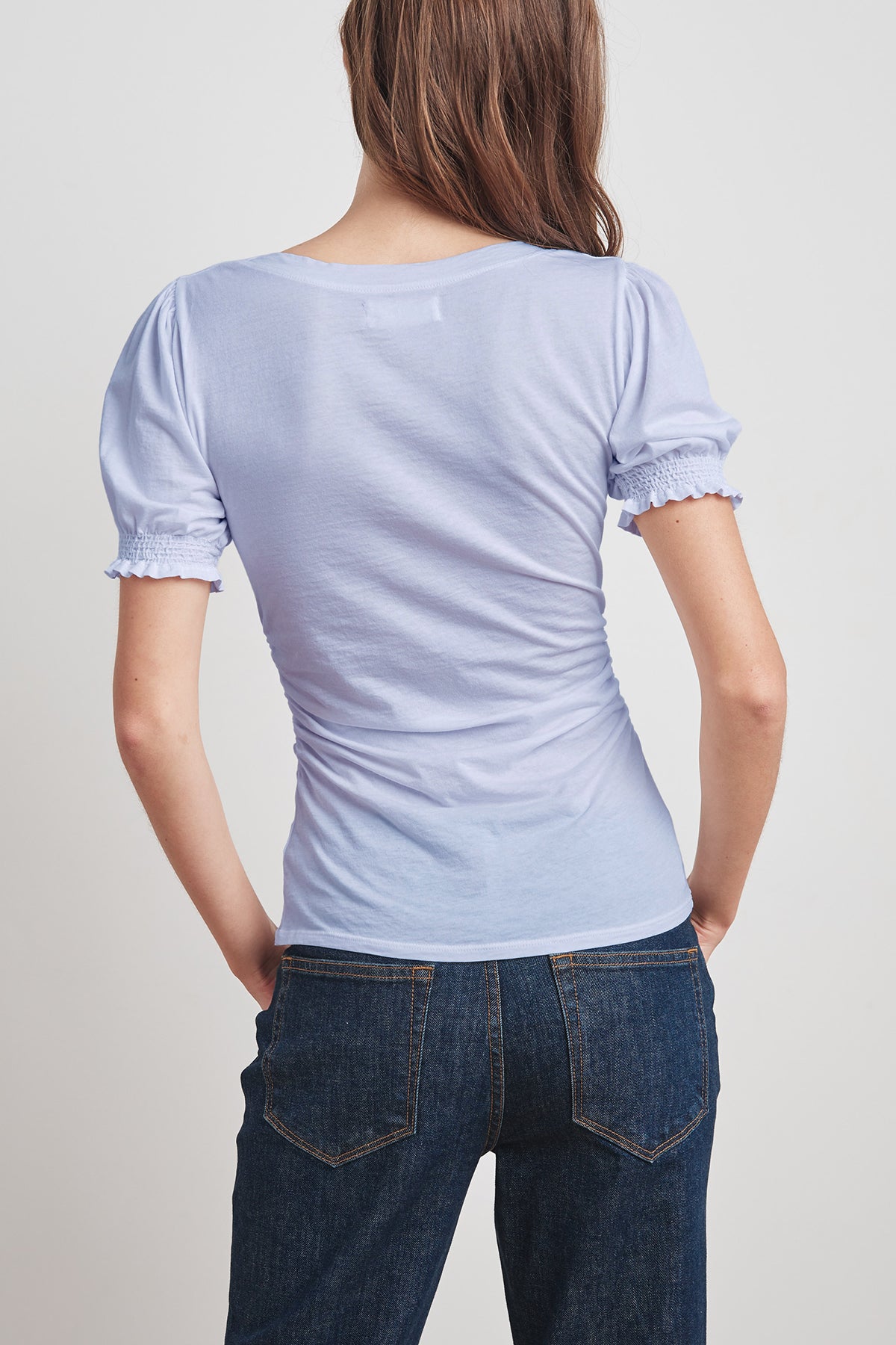 Person with long hair wearing a light blue, short-sleeved Velvet by Graham & Spencer KAMI GAUZY WHISPER SHIRRED SLEEVE TOP and dark denim jeans, viewed from the back.