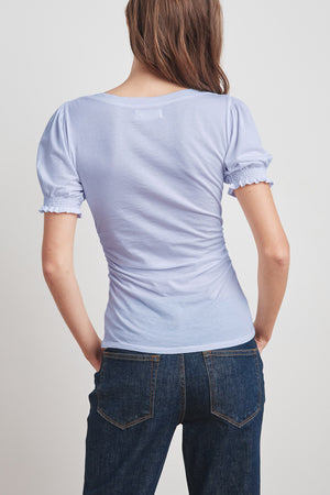 Person with long hair wearing a light blue, short-sleeved Velvet by Graham & Spencer KAMI GAUZY WHISPER SHIRRED SLEEVE TOP and dark denim jeans, viewed from the back.